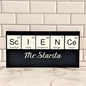 May include: Black and white sign with the word "SCIENCE" spelled out using the chemical symbols for Scandium, Iodine, Einsteinium, Nitrogen, and Cerium. The sign also includes the text "Mr. Starita".
