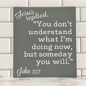 May include: A gray wooden sign with white text that reads "Jesus replied, "You don't understand what I'm doing now, but someday you will." John 13.7"