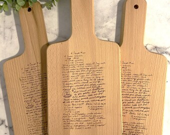 May include: Three wooden cutting boards with a handle, each engraved with handwritten text. The boards are light brown with a smooth finish and a hole for hanging. The text appears to be a recipe for a pie.