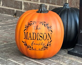 Puede incluir: Una calabaza naranja con el texto "the MADISON family" en letras negras. La calabaza está sentada sobre una superficie de ladrillo.