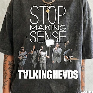 May include: A charcoal grey acid-wash t-shirt featuring the white text STOP MAKING SENSE and TALKING HEADS. The graphic includes a photograph of a musical band performing on stage with instruments and microphones. The shirt has a crew neck and short sleeves.