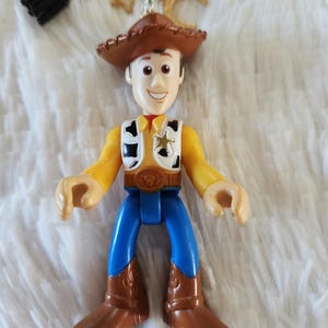 May include: A brown cowboy hat with a yellow star sheriff badge on a toy figurine of Woody from Toy Story. The figurine is wearing a blue shirt, blue jeans, and brown cowboy boots.