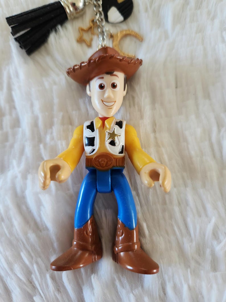 May include: A brown cowboy hat with a yellow star sheriff badge on a toy figurine of Woody from Toy Story. The figurine is wearing a blue shirt, blue jeans, and brown cowboy boots.