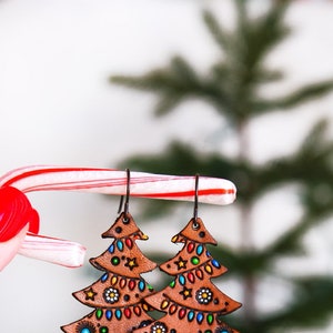 May include: A pair of brown leather Christmas tree earrings with colorful painted details, including lights, stars, and ornaments.