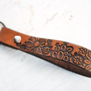 May include: A brown leather keychain with a floral design. The keychain has a metal ring for attaching keys.