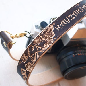 May include: A brown leather camera strap with a floral design and the name "KAYZAKIAN" embossed in gold lettering.