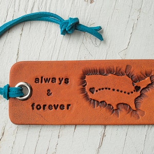 May include: A brown leather bookmark with a map of the United States and the words "always & forever" embossed on it. The bookmark has a teal leather cord attached to it.