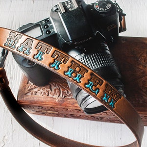 May include: A brown leather camera strap with the name "MATTHEW" embossed in blue lettering.