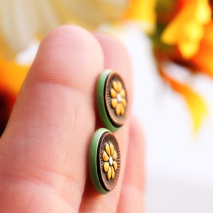May include: A pair of green and brown stud earrings with a yellow flower design.