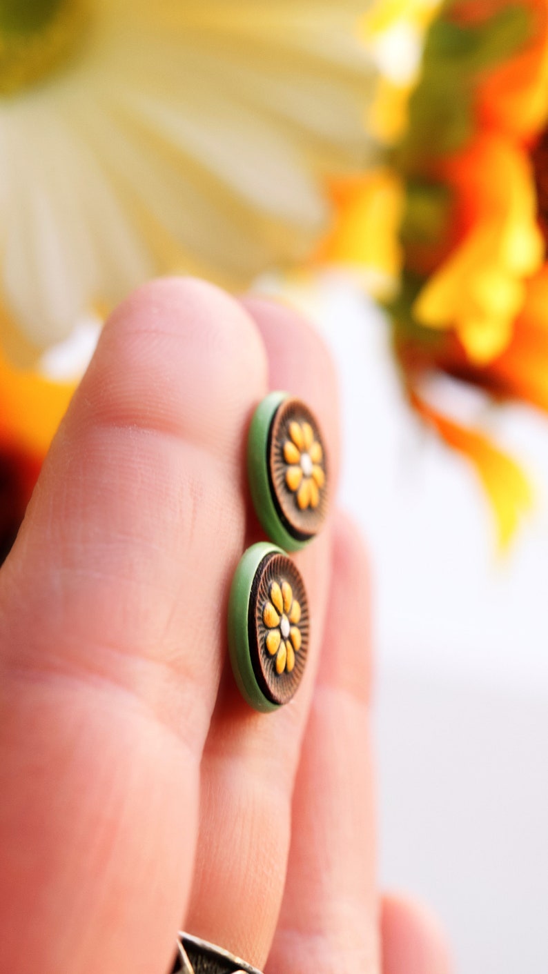 May include: A pair of green and brown stud earrings with a yellow flower design.