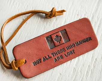 Pode incluir: Uma etiqueta de bagagem de couro marrom com uma bandeira canadense e o texto "Not all those who wander are lost".