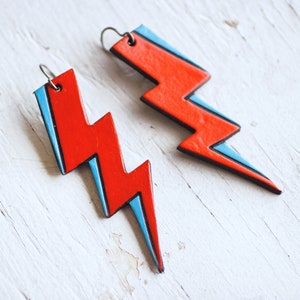 May include: A pair of red and blue lightning bolt shaped earrings. The earrings are made of leather and have a silver hook.