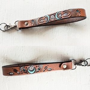 May include: A brown leather key chain with a turquoise and white moon and flower design. The key chain has a silver swivel clasp.