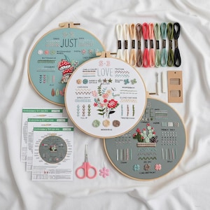 以下が含まれることがあります： さまざまなステッチ例とデザインが施された、3つの丸い刺繍枠が入った刺繍キット。 キットには、さまざまな色の刺繍糸、針、ハサミ、説明書が含まれています。 刺繍枠には「JUST」と「LOVE」という文字が書かれています。