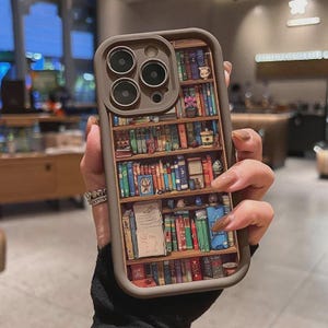 May include: A brown phone case featuring a detailed bookshelf design. The case has a dark brown border and a 3D rendering of a wooden bookshelf filled with colorful books, small plants, and decorative items.