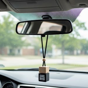 Könnte beinhalten: Ein schwarzer Auto-Lufterfrischer, der am Rückspiegel hängt. Der Lufterfrischer hat einen Holzquader auf einem schwarzen Quader, mit dem Text "Relaxing Car Diffuser". Das Armaturenbrett und die Windschutzscheibe des Autos sind sichtbar.