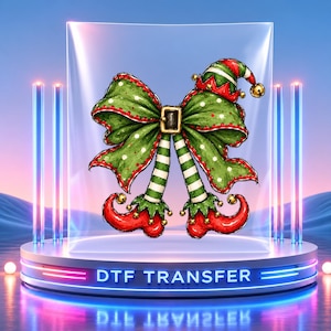 May include: A DTF transfer graphic featuring a green polka-dot bow with a black belt buckle center, topped with a red and green elf hat with a gold bell, and two dangling green and white striped elf legs with red curled shoes.