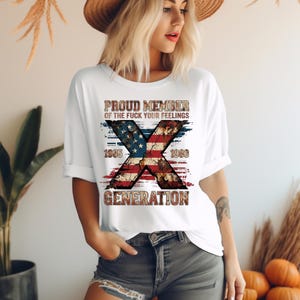 May include: A white short-sleeved t-shirt featuring a large graphic of a distressed American flag in the shape of an X. The text reads PROUD MEMBER OF THE FUCK YOUR FEELINGS 1965 1980 GENERATION in a weathered, brown, and textured font style.