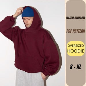 May include: A burgundy oversized hoodie with a kangaroo pocket. The person in the image is wearing a blue beanie. The image includes the text "INSTANT DOWNLOAD", "PDF PATTERN", "OVERSIZED HOODIE", and "S - XL".