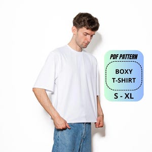 Peut inclure: Un t-shirt blanc uni à manches courtes avec une coupe carrée et un col rond. Un graphique numérique superposé sur la droite affiche le texte PDF PATTERN BOXY T-SHIRT S - XL dans un cadre rectangulaire arrondi avec un fond dégradé.