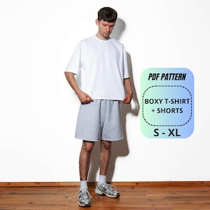 May include: A white boxy t-shirt and grey shorts set. A graphic overlay displays the text PDF PATTERN, BOXY T-SHIRT + SHORTS, and S - XL. The clothing features a loose, relaxed fit with short sleeves and knee-length shorts, presented as a digital pattern.