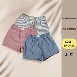 May include: Three pairs of sleep shorts in red, blue, and gray with vertical stripes. The shorts have an elastic waistband and a small tag. The image also includes the text "INSTANT DOWNLOAD", "PDF PATTERN", "SLEEP SHORTS", and "S - XL".