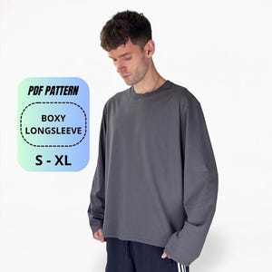 Op de afbeelding: Een donkergrijs shirt met lange mouwen en een boxy pasvorm. Een rechthoekige afbeelding met een verloopachtergrond toont de tekst PDF PATTERN, BOXY LONGSLEEVE en S - XL. Het shirt heeft een ronde hals en wijde mouwen, als digitaal naaipatroon.