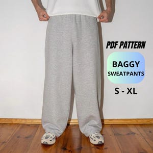 Puede incluir: Pantalones de chándal gris claro holgados con corte ancho. La imagen incluye el texto PDF PATTERN BAGGY SWEATPANTS S - XL. Los pantalones se combinan con una camiseta blanca lisa y zapatillas deportivas claras sobre un suelo de madera.