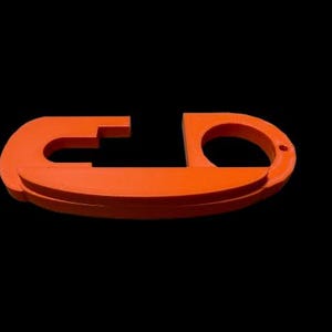 May include: An orange plastic key holder with a unique design. The holder has a loop on one end and a flat surface on the other.