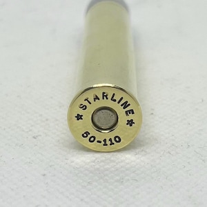May include: Close-up of a brass bullet casing with the text "STARLINE" and "50-110" stamped on the base. The bullet has a silver primer and a gold-colored casing. The casing is cylindrical with a rounded tip.