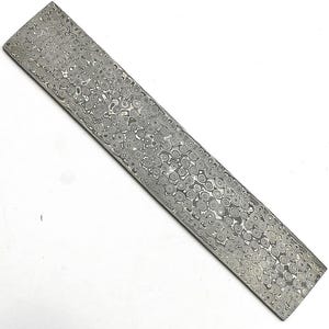 May include: A rectangular metal billet featuring a complex, multi-layered Damascus steel pattern. The surface displays a dense, repeating arrangement of swirling, organic gray and silver metallic shapes across the entire flat face.