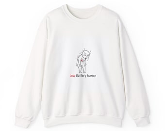 Puede incluir: Sudadera blanca de cuello redondo con un gráfico negro y rojo de un muñeco de palo con un símbolo de batería baja. El texto "Low Battery human" está debajo. La sudadera tiene mangas largas.