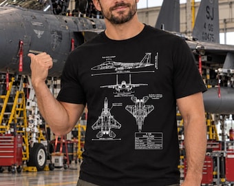May include: A black t-shirt featuring a white technical blueprint graphic of an F-15E Strike Eagle fighter jet. The design includes detailed line drawings, side and top views, and technical specifications with measurements in feet and inches.