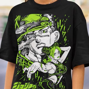 May include: Black t-shirt featuring a graphic design with a manga-style illustration in shades of green and white. The design includes a male figure and a female figure, along with Japanese text. The shirt is worn by a person wearing sunglasses.
