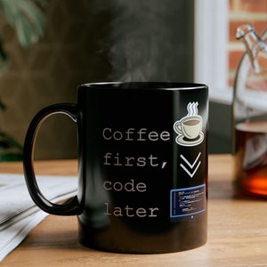Op de afbeelding: Zwarte koffiemok met witte tekst die "Coffee first, code later" luidt. De mok heeft een klein wit koffiekopje-icoon met stoom die eruit komt en een vinkje. Er is ook een klein icoon van een computerscherm met code erop.