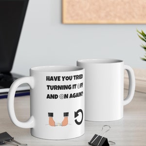 Könnte beinhalten: Weiße Keramiktasse mit schwarzem Text, der "Haben Sie es versucht, aus- und wieder einzuschalten?" lautet, mit einer Cartoon-Illustration von Händen, die einen Netzschalter ein- und ausschalten, und einem Aktualisierungspfeil.