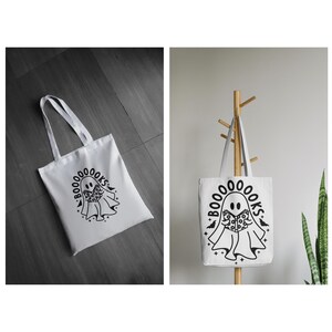 Pu&ograve; includere: Borsa tote bianca con un'illustrazione in bianco e nero di un fantasma che tiene un libro. Il testo "BOO00000KS" &egrave; scritto intorno al fantasma.