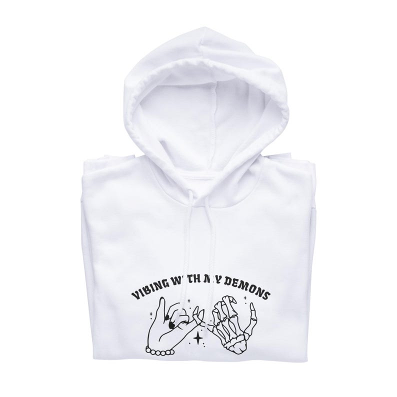 May include: White hooded sweatshirt with a black graphic print of two hands holding pinky fingers. The text "VIBING WITH MY DEMONS" is printed in black above the hands.