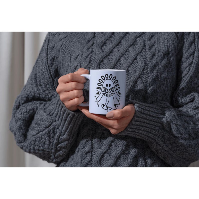 Pu&ograve; includere: Tazza in ceramica bianca con un'illustrazione in bianco e nero di un fantasma che legge un libro. Il testo intorno al fantasma dice "Boo-ooks".