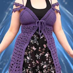 May include: A purple crochet top with a halter neck and open front design. The top features decorative shoulder straps and a tie closure at the bust. The top is worn over a black tank top and a black floral print skirt.