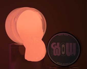 Könnte beinhalten: Ein Glas mit rosa, im Dunkeln leuchtendem Schleim mit dem Text "That Glow" und "Rose Pink" auf dem Deckel.