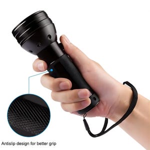 Puede incluir: Linterna negra con un mango texturizado para agarre, sostenida en una mano. La linterna tiene una correa para la muñeca y una vista detallada del diseño antideslizante. El texto en la imagen dice "Antislip design for better grip."
