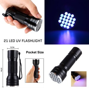 K&ouml;nnte beinhalten: Schwarze 21 LED UV-Taschenlampe, 9,4 cm lang und 3 cm breit, mit strukturiertem Griff und silberner L&uuml;nette. Das Bild zeigt die Taschenlampe in Gebrauch, die ein helles violettes Licht aussendet. Der Text lautet "21 LED UV FLASHLIGHT" und "Pocket Size."