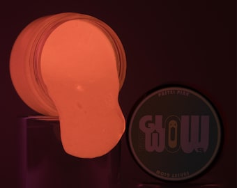 Könnte beinhalten: Ein Glas mit pastellrosa leuchtendem Schleim mit dem Text "GLOW" und "MOJO TREASURES" auf dem Deckel.