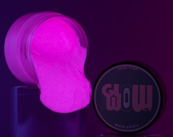 Könnte beinhalten: Ein Glas mit neonrosa Schleim und einem schwarzen Deckel, auf dem in weißer Schrift "Glow in the Dark Violet Glow Neon Pink" steht.