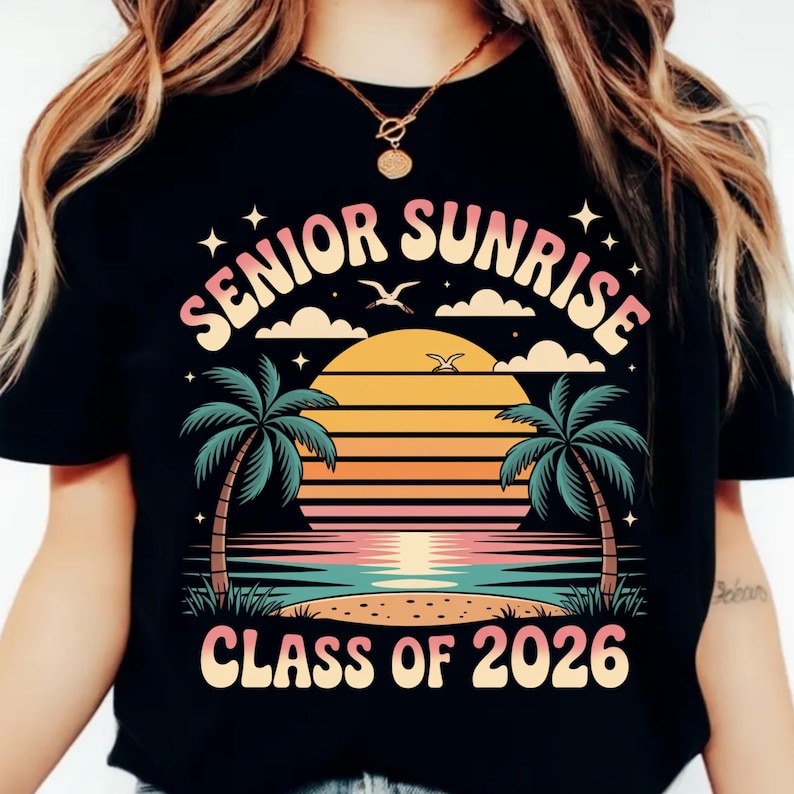 K&ouml;nnte beinhalten: Schwarzes T-Shirt mit einem farbenfrohen Grafikdesign. Das Design zeigt die Worte "SENIOR SUNRISE" in einer Retro-Schriftart &uuml;ber einer Sonnenuntergangsszene mit Palmen, Wolken und dem Text "CLASS OF 2026".