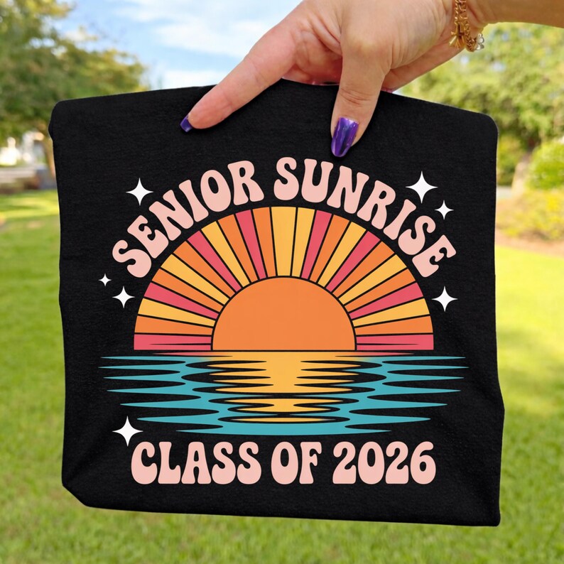 K&ouml;nnte beinhalten: Schwarzes T-Shirt mit einem Retro-Sonnenuntergang-Design. Das Design enth&auml;lt die W&ouml;rter "SENIOR SUNRISE" und "CLASS OF 2026". Der Sonnenuntergang zeigt eine orangefarbene Sonne, gelbe und orangefarbene Strahlen und blaues Wasser.