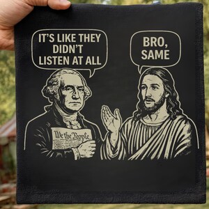 May include: Black square decorative sign featuring illustrations of George Washington and Jesus Christ. Speech bubbles above them read "It's like they didn't listen at all" and "Bro, Same". Washington holds a document that says "We the People".