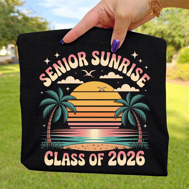 K&ouml;nnte beinhalten: Schwarzes T-Shirt mit einem farbenfrohen Grafikdesign. Das Design zeigt den Text "SENIOR SUNRISE CLASS OF 2026" &uuml;ber einer Sonnenuntergangsszene mit Palmen, Wolken und V&ouml;geln. Das Design ist in Orange-, Rosa- und Blaut&ouml;nen gehalten.