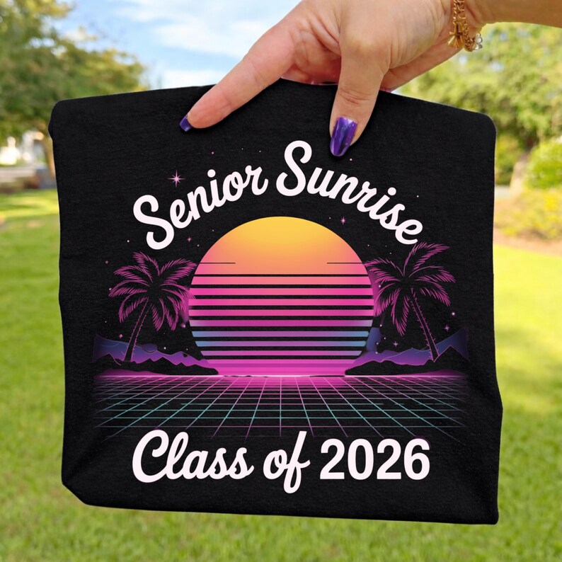 K&ouml;nnte beinhalten: Schwarzes T-Shirt mit einem Retro-Design mit Sonnenuntergang, Palmen und einem Rastermuster. Der Text "Senior Sunrise" und "Class of 2026" ist in Wei&szlig;. Das Design hat ein lebendiges Farbschema aus Orange, Pink, Lila und Blau.